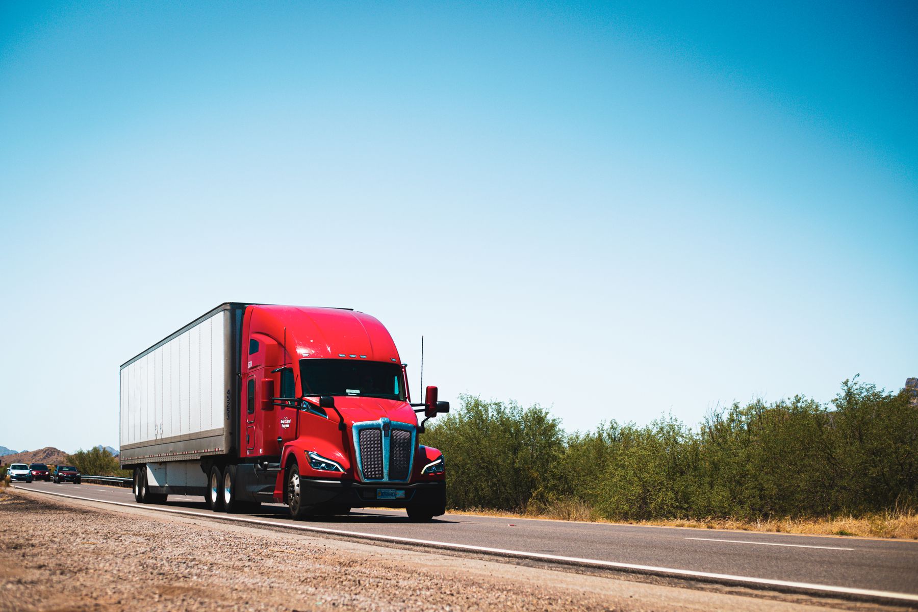 Red American semi truck with a dry van trailer traveling along an open road