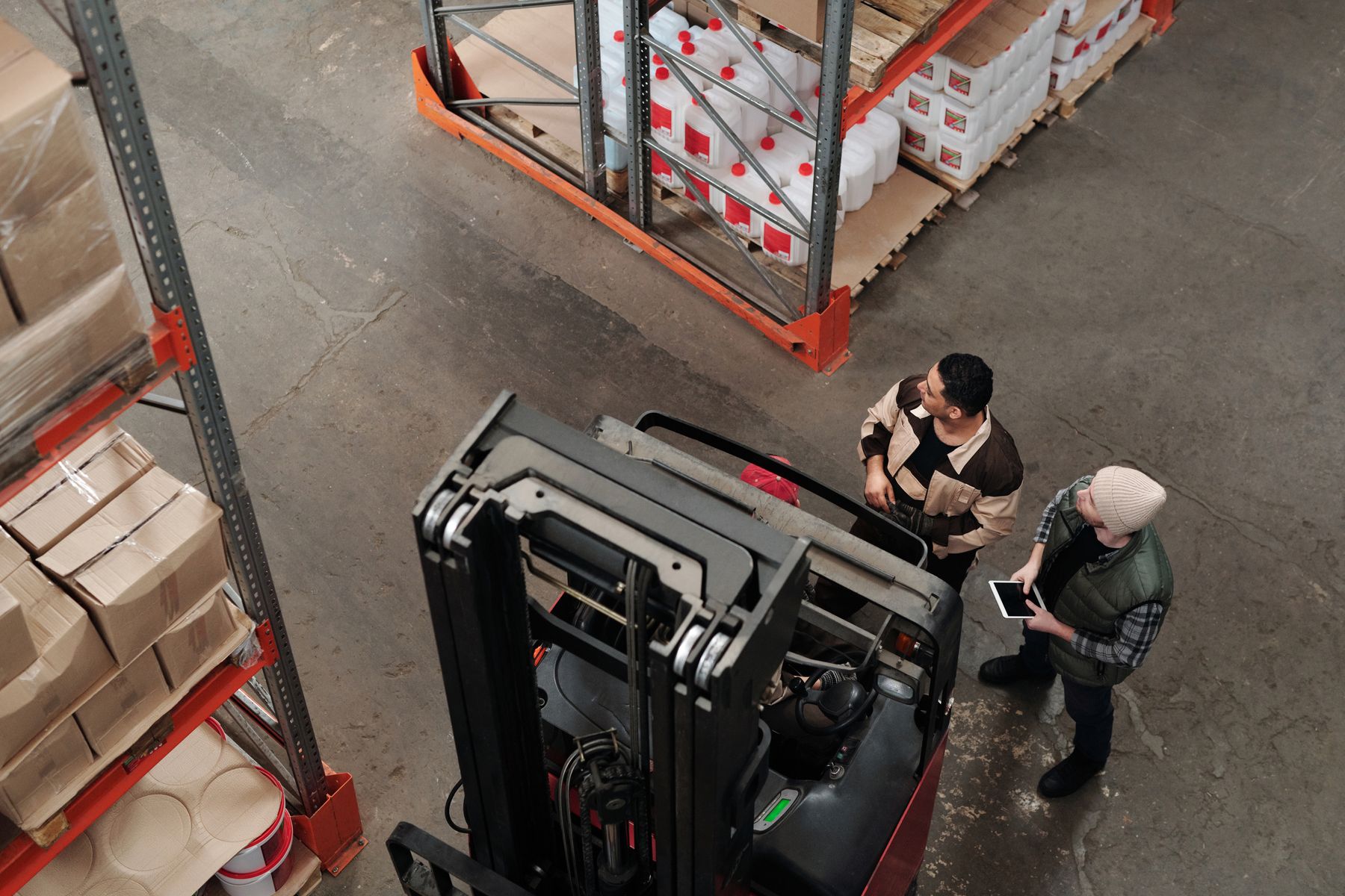 Two warehouse staff discussing work beside a forklift, viewed from above
